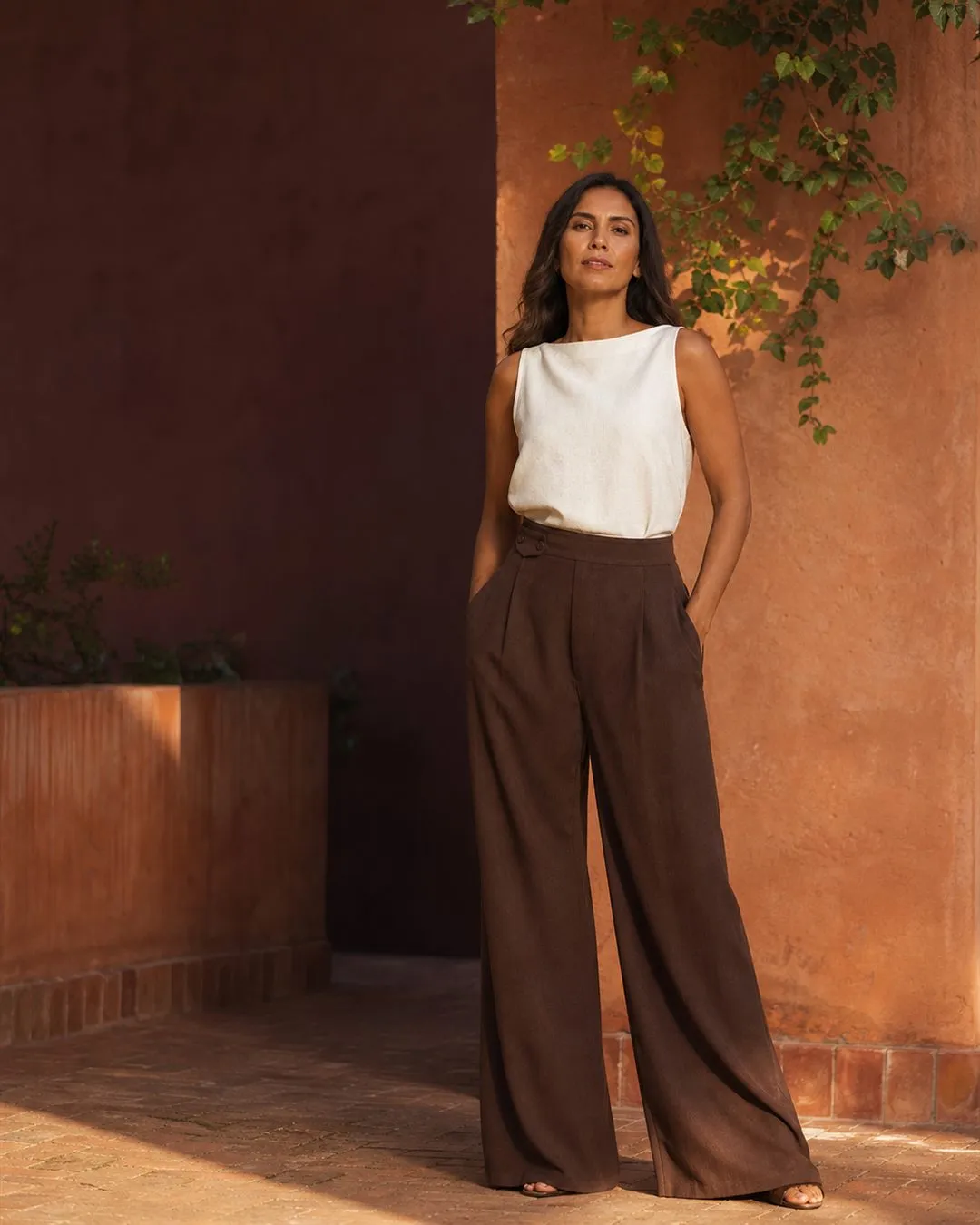 Mujer adulta con pantalón amplio color cacao y blusa marfil en un patio de tonos terracota